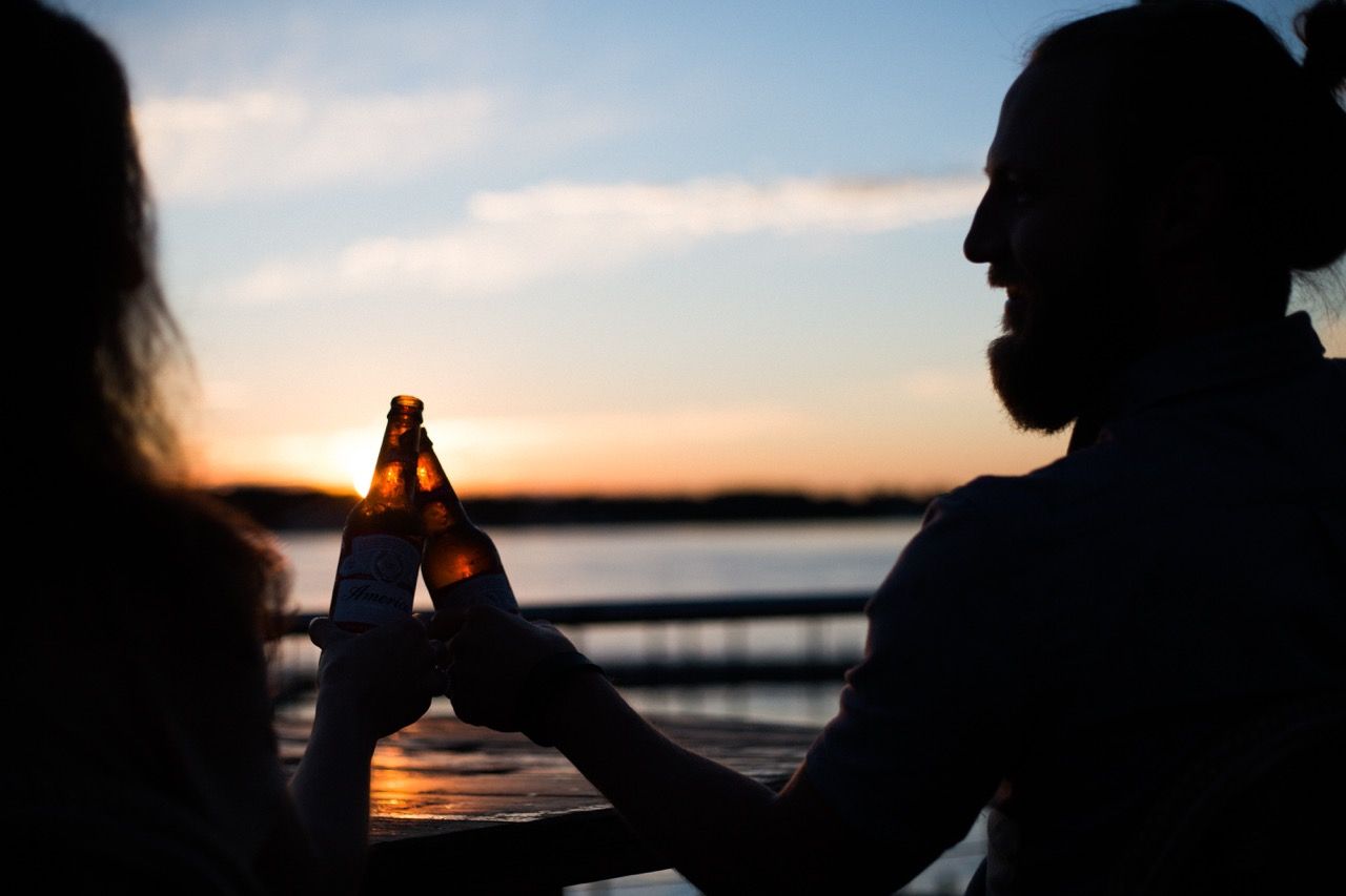 Two people sharing a beer over by the water at sunset.