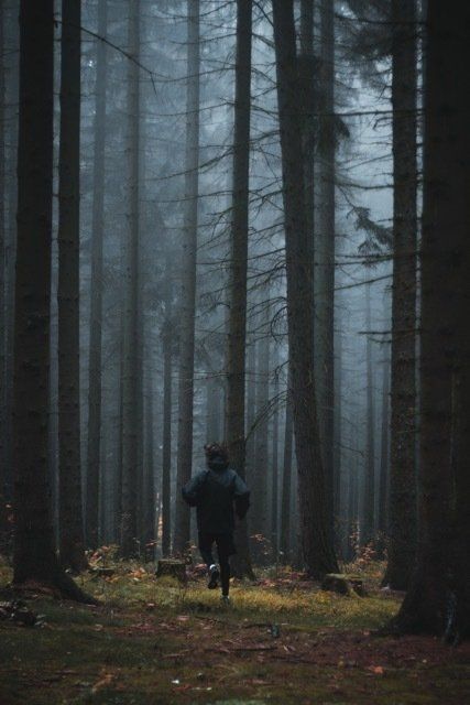 Person running through trees in a woodland.