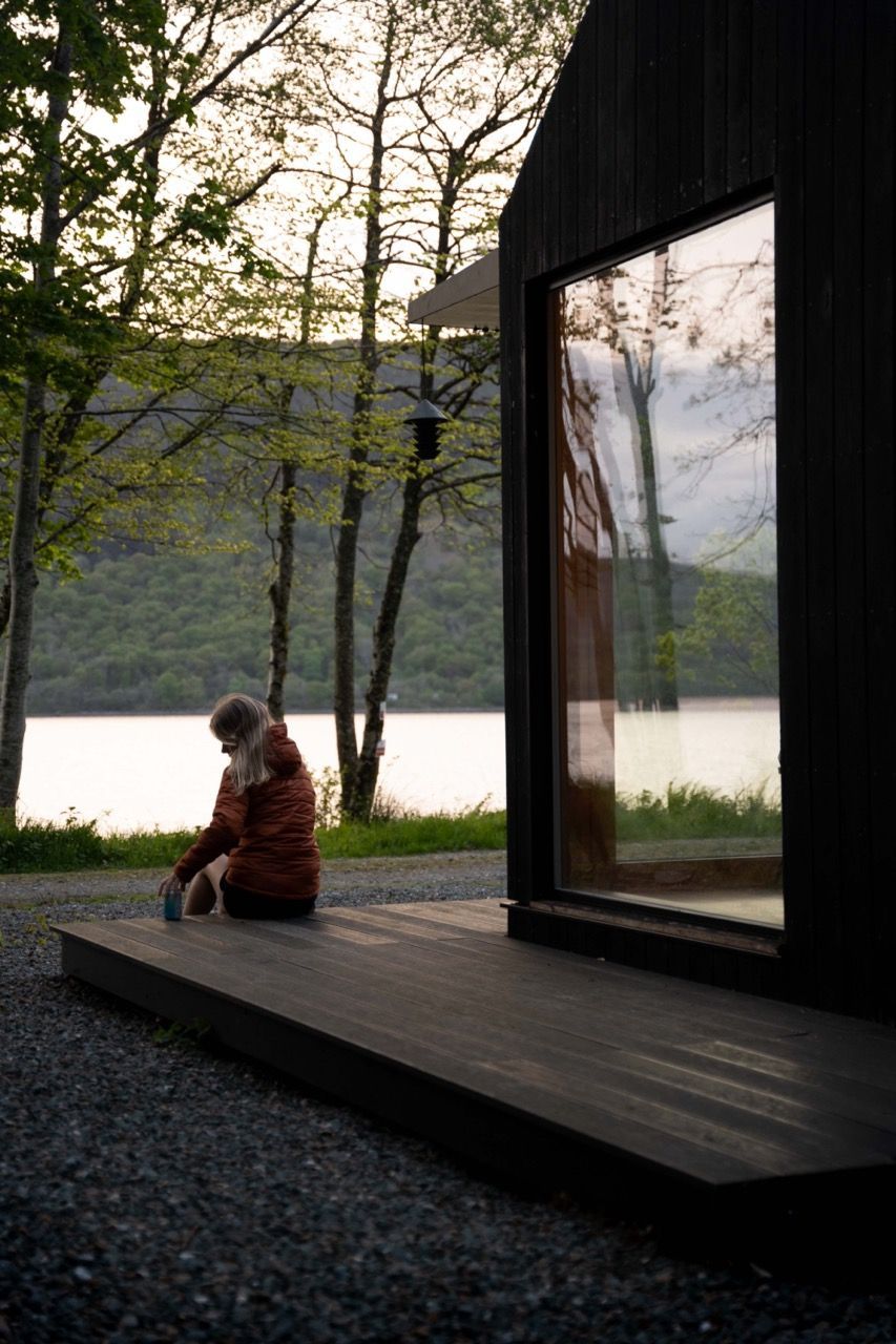 Female drinking a beer at a black cabin looking out to water.