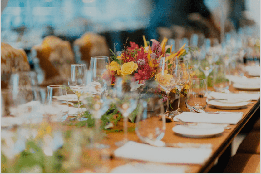 Long set table with flowers glasses and plates on it.
