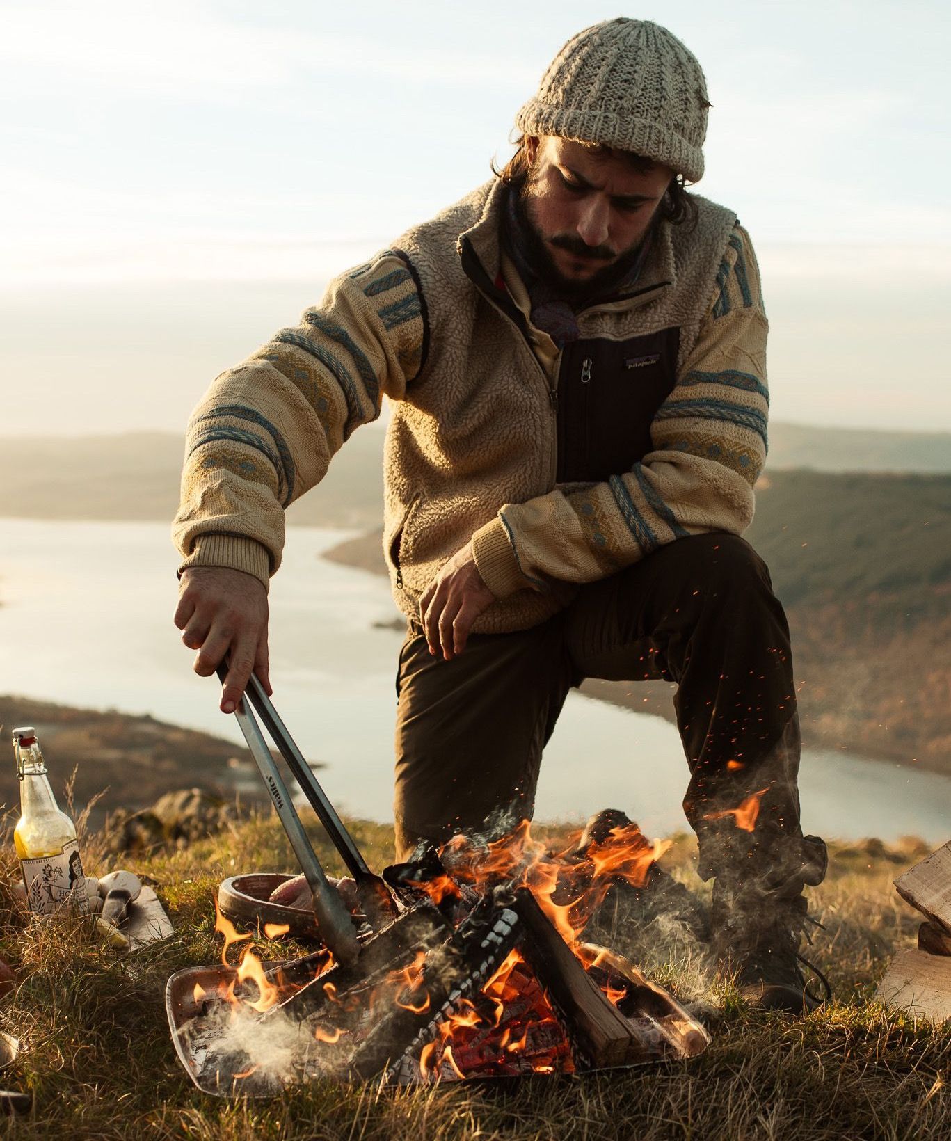 Chef preparing scallops over an open fire on a pebble beach.