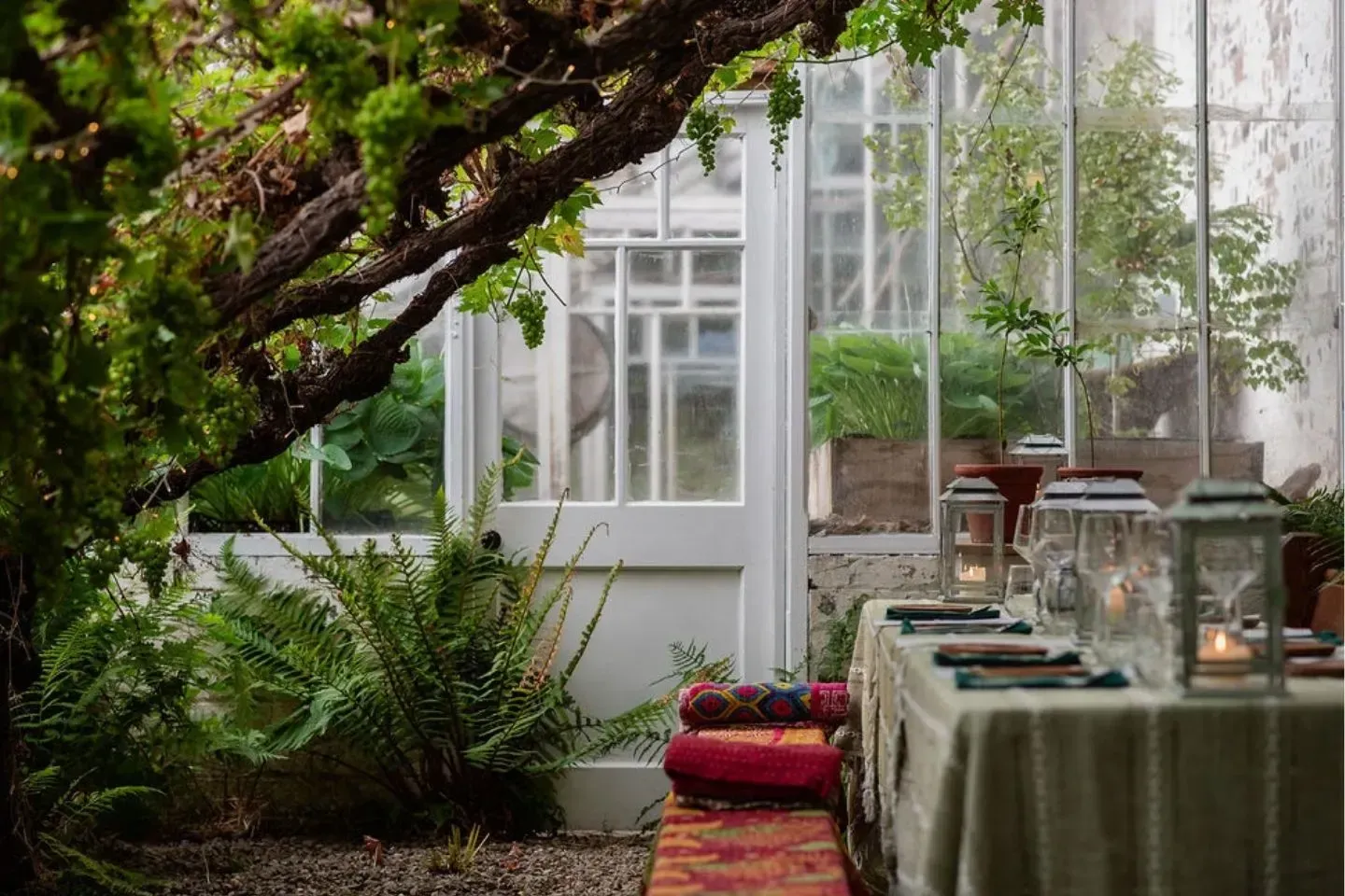 A romantic dining experience in a greenhouse, with greenery and lanterns, and a white framed door Kabn.
