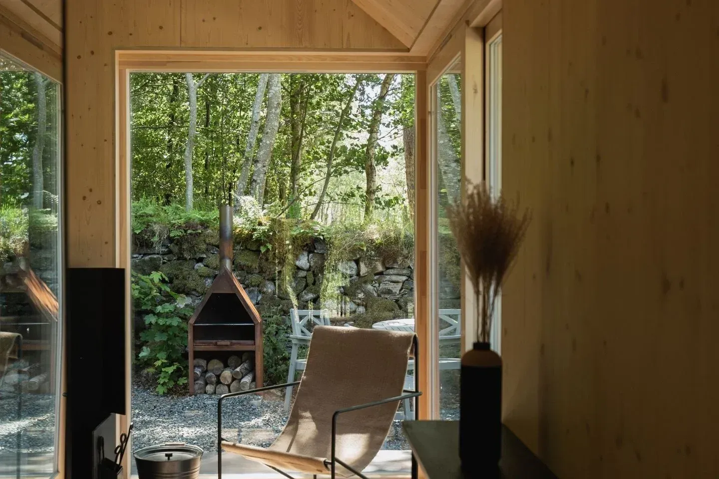 Minimalist cabin interior design with floor-to-ceiling glass windows overlooking a forest and a modern wood-burning stove.