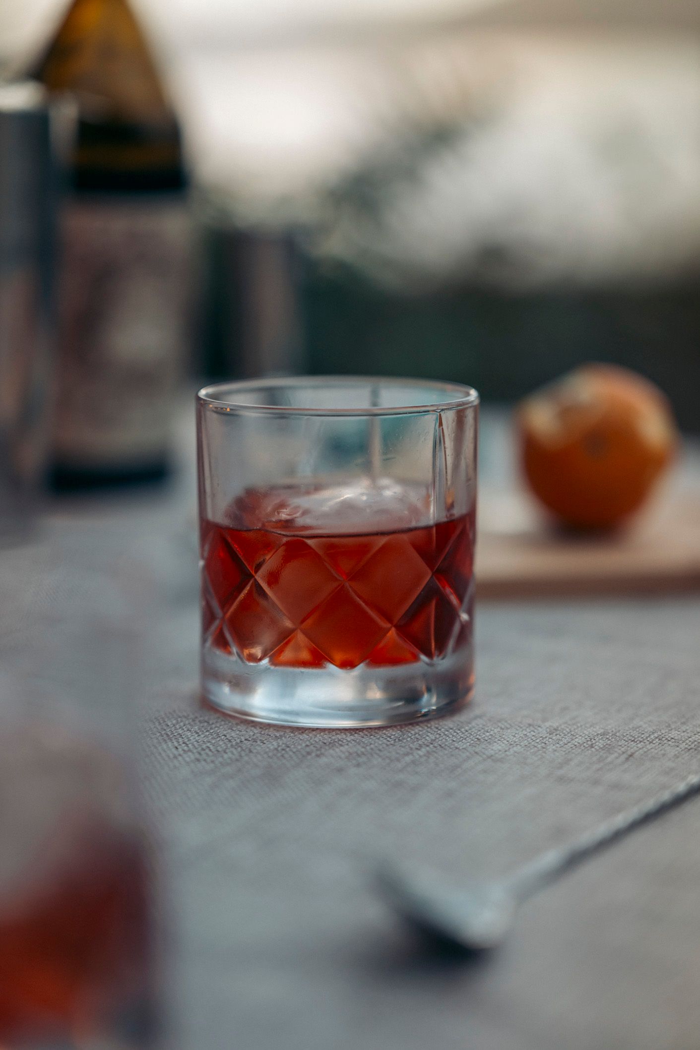 Close-up of a cocktail in a patterned glass, with an orange and bar spoon on a table.