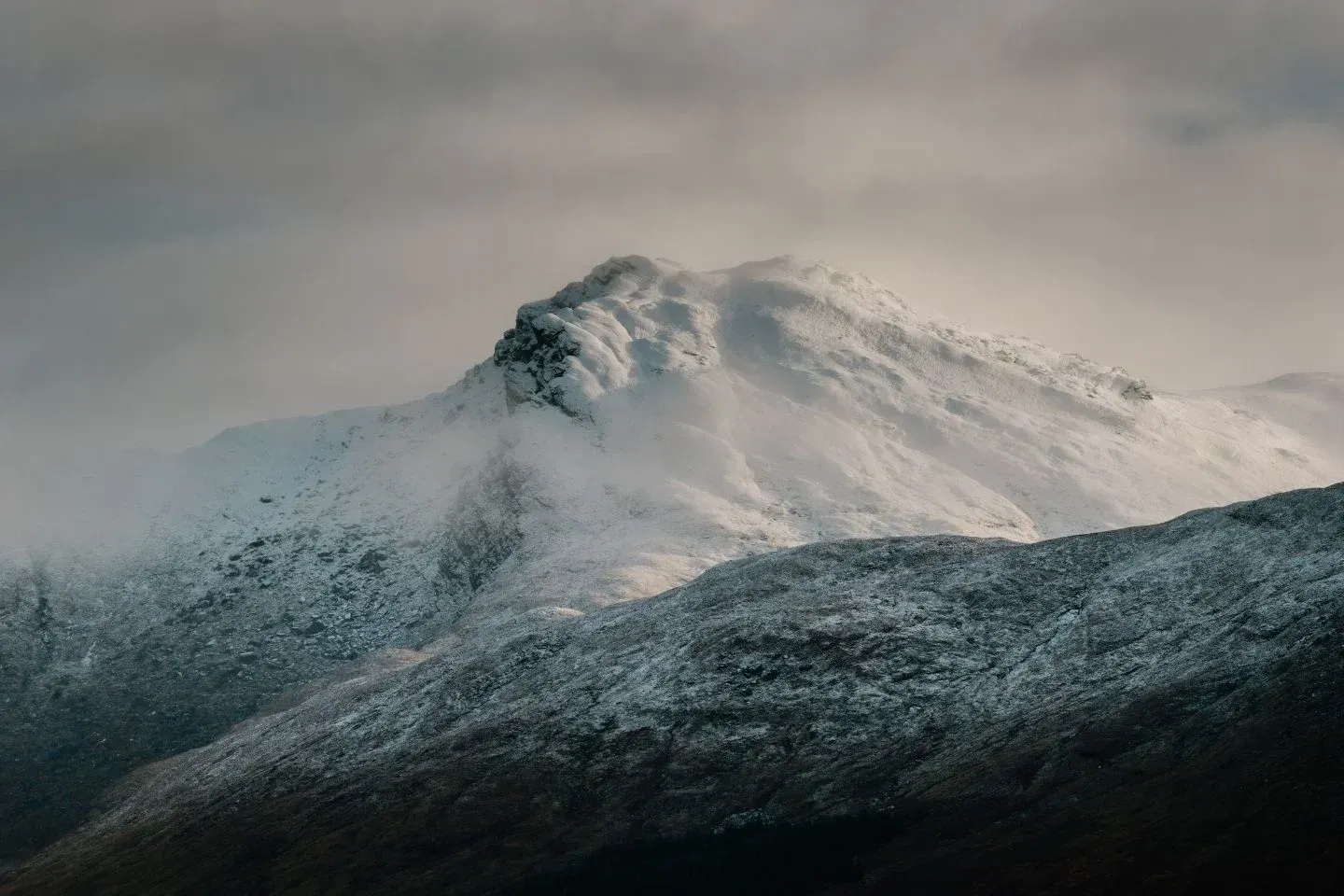 Dramatic aerial view of snowy mountain peaks near Loch Fyne, showcasing the rugged Scottish Highlands landscape.
