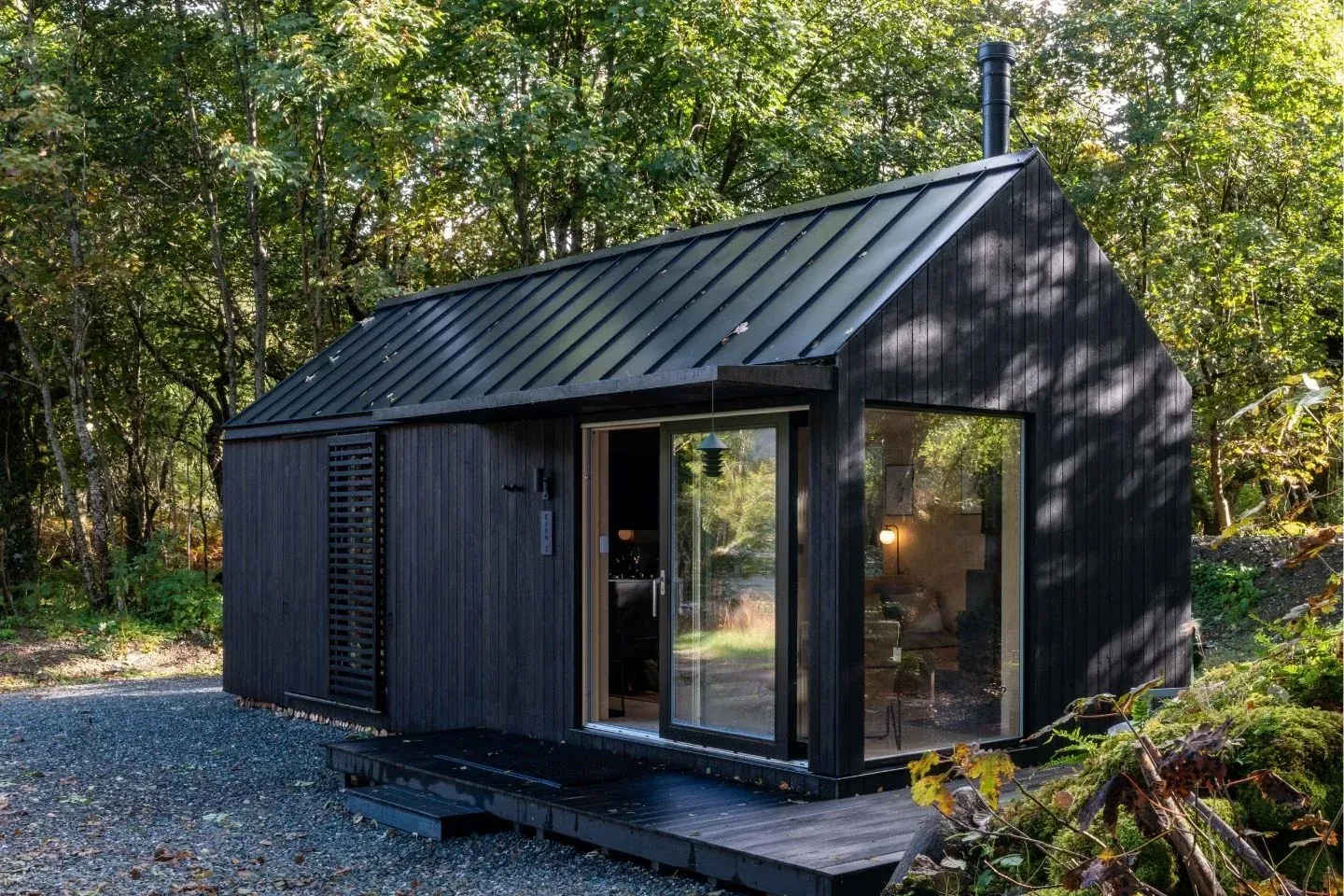 Modern black corrugated metal cabin design with large glass doors, an eco-friendly luxury stay in nature.