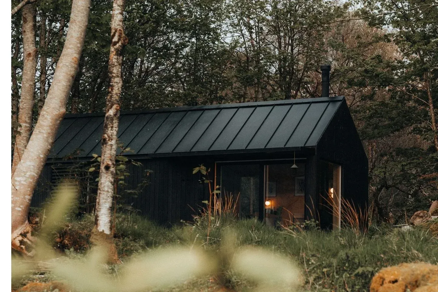 Secluded black timber cabin nestled in a lush Scottish forest, a luxury nature hideaway for remote stays.