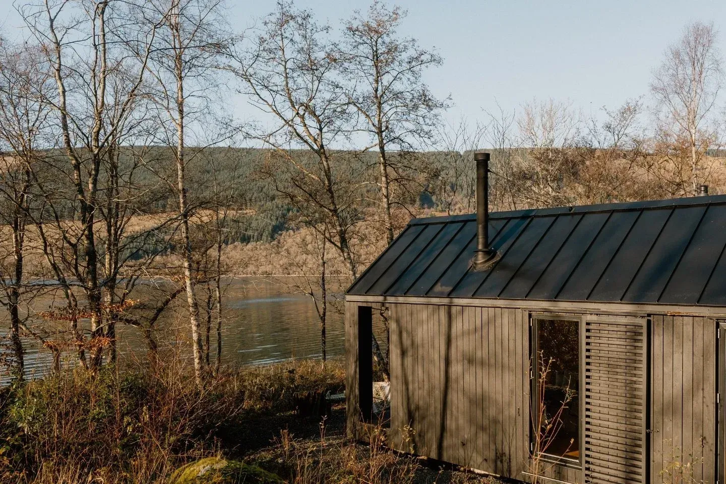 Off-grid cabin exterior during autumn with golden trees and a view of the water in the background.