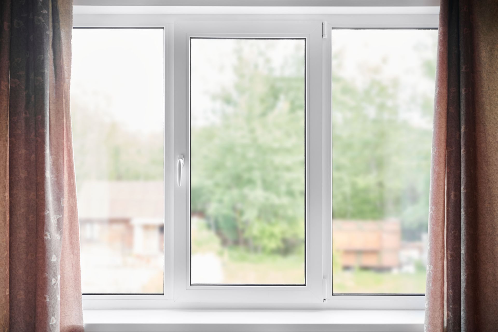 White-framed window with view of blurred green trees and a building; brown curtains frame the window.