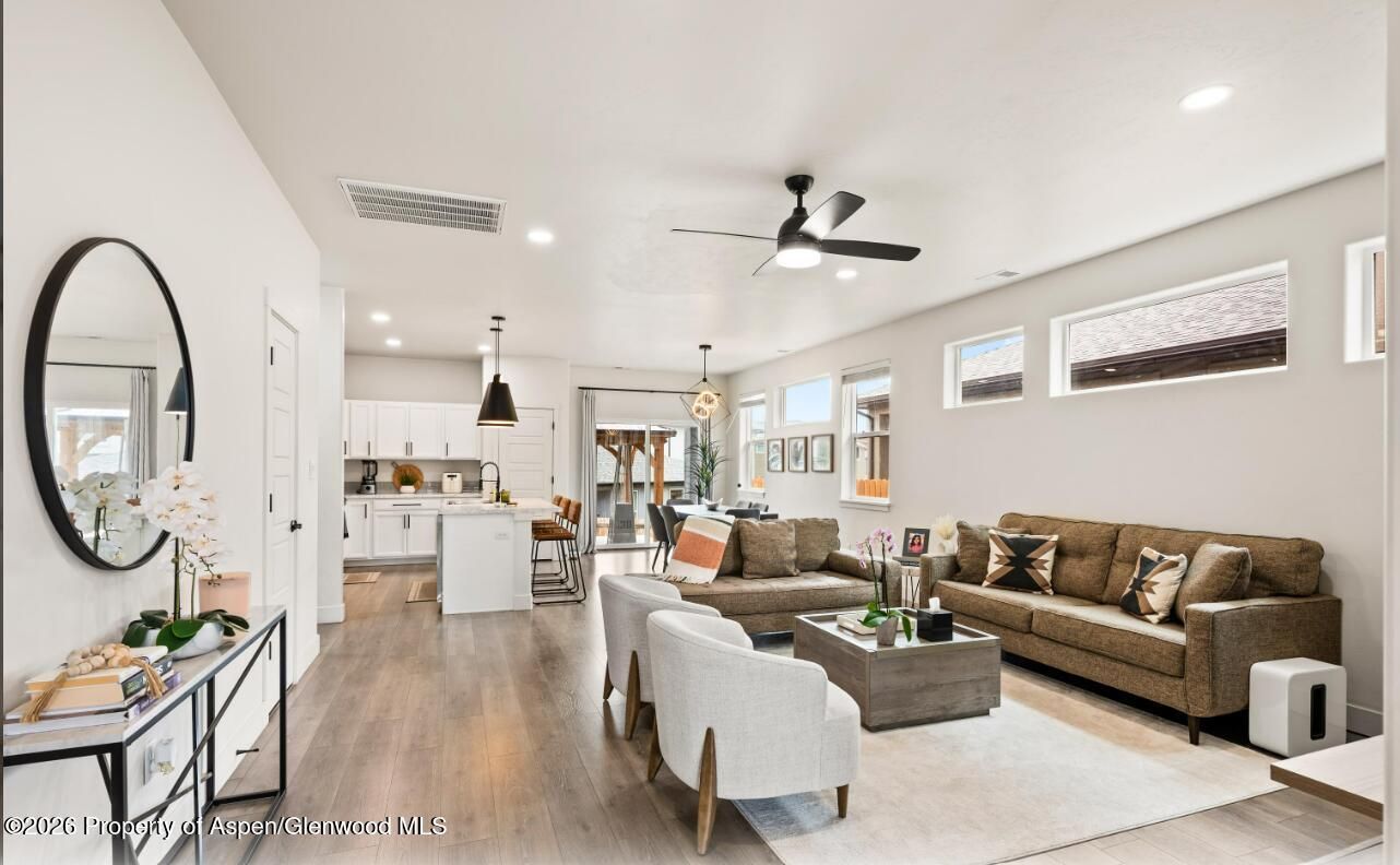 Bright open-concept living room with beige sofas, round mirror, fireplace, and ceiling fan in a modern home