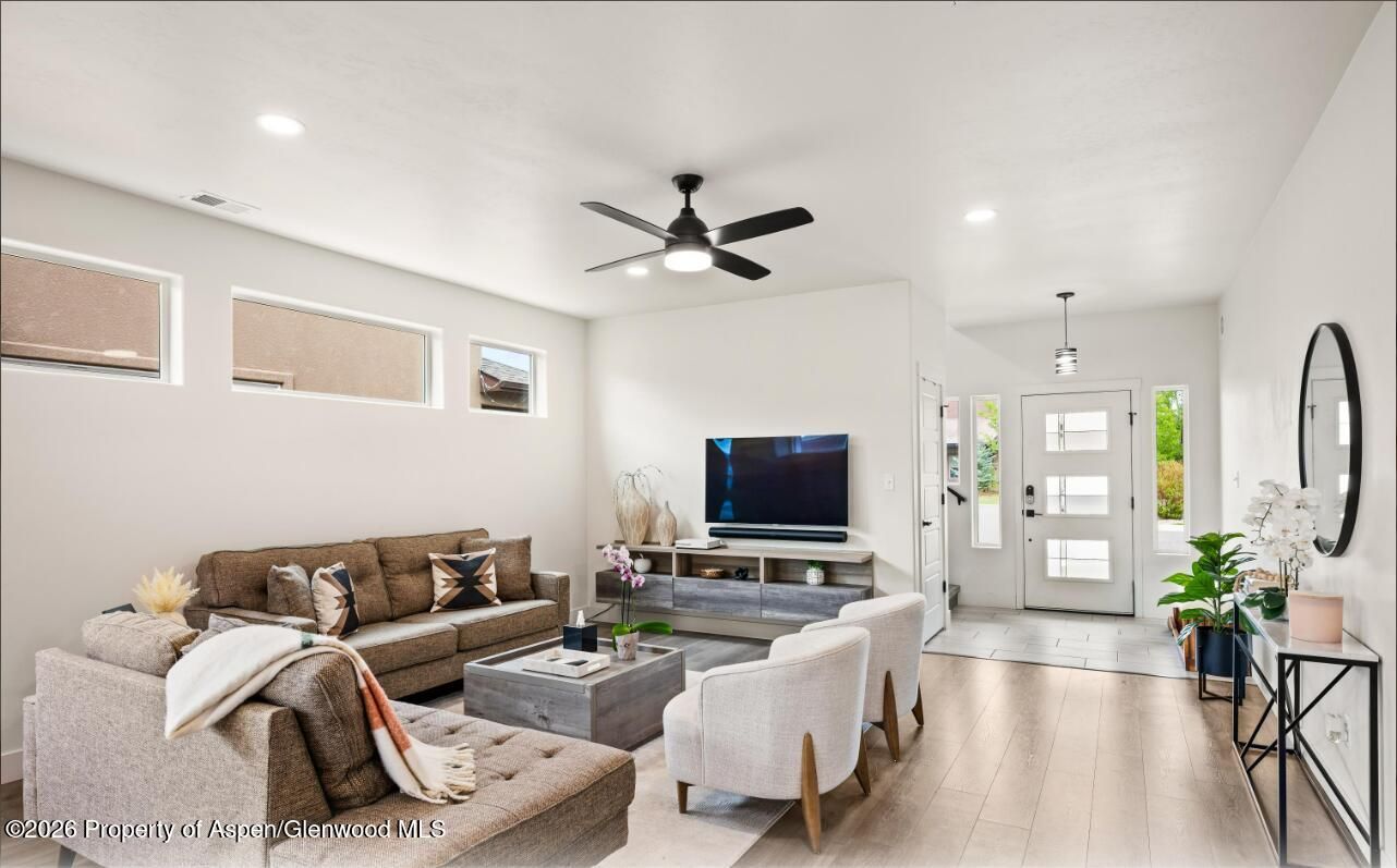 Bright modern living room with sectional sofa, TV, white chair, ceiling fan, and front door.