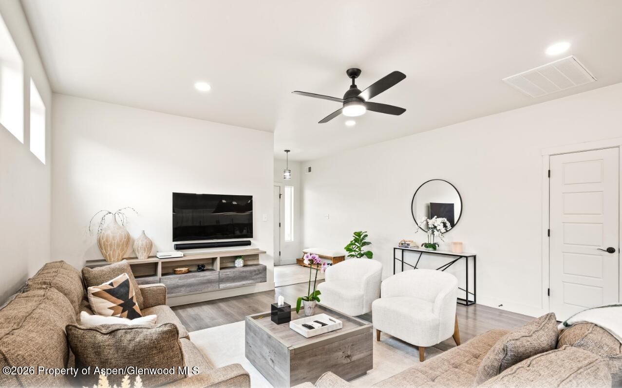Bright modern living room with white walls, ceiling fan, TV, gray sofa, and coffee table
