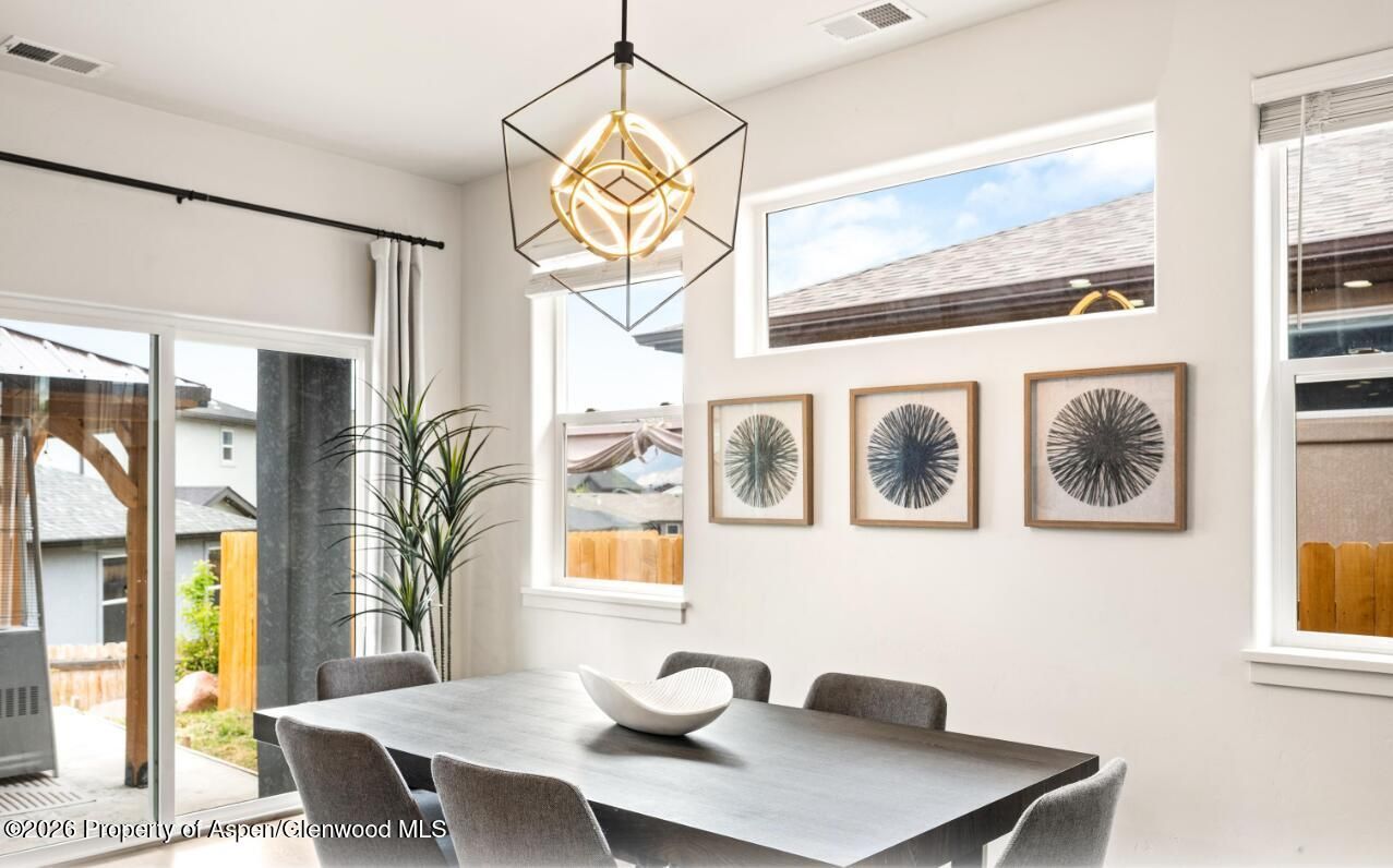 Modern dining room with large windows, gray table and chairs, pendant light, and framed wall art.