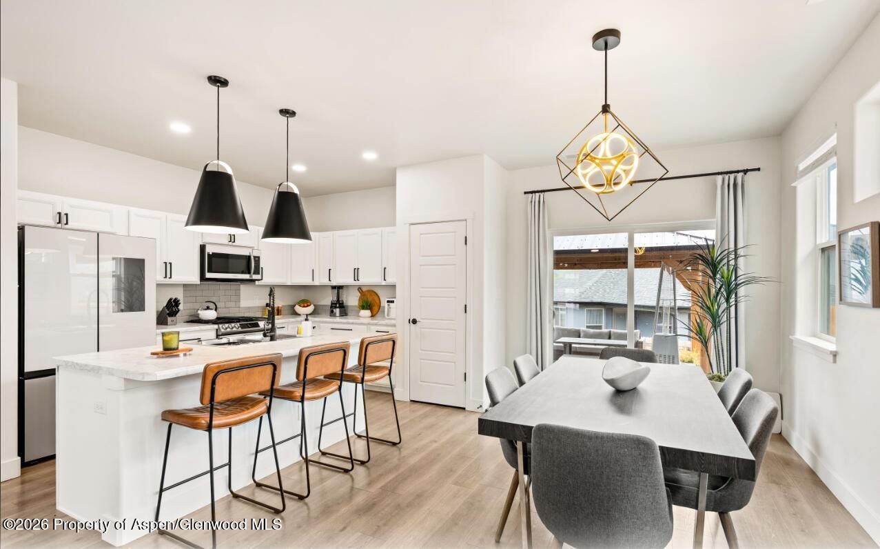 Bright modern kitchen and dining area with white cabinets, island stools, and a large dining table by sliding doors