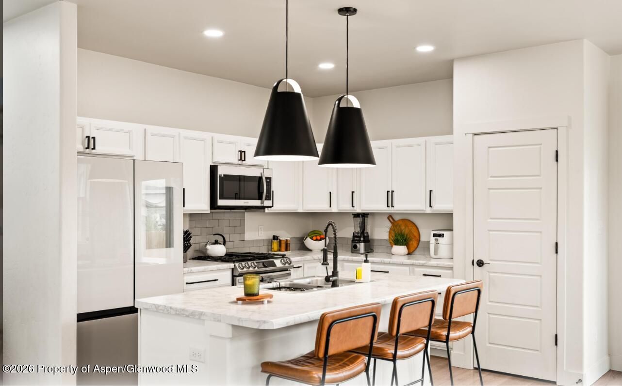 Bright white kitchen with island, black pendant lights, stainless appliances, and two brown bar stools