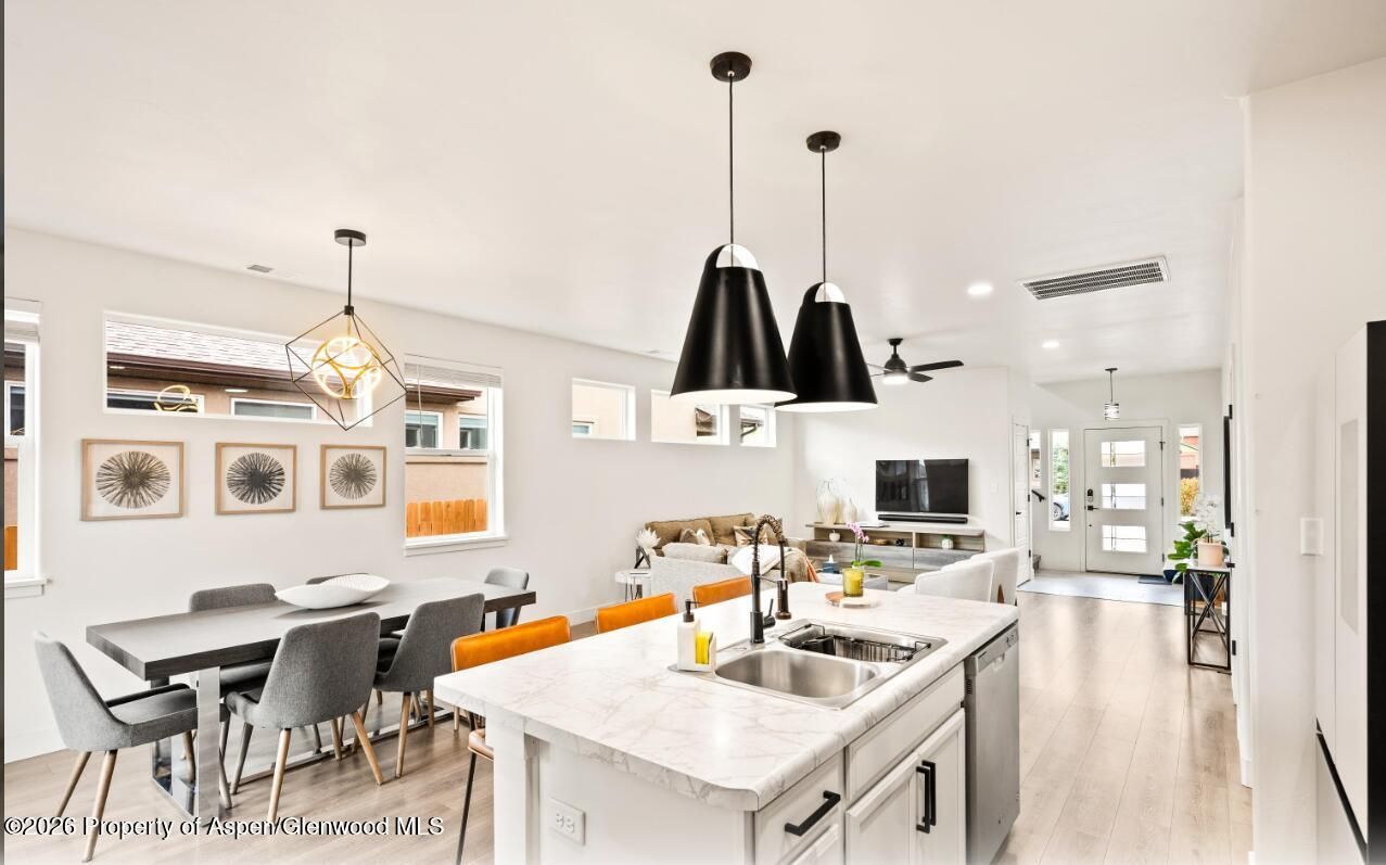Bright modern kitchen with white island, black pendant lights, orange bar stools, and dining area