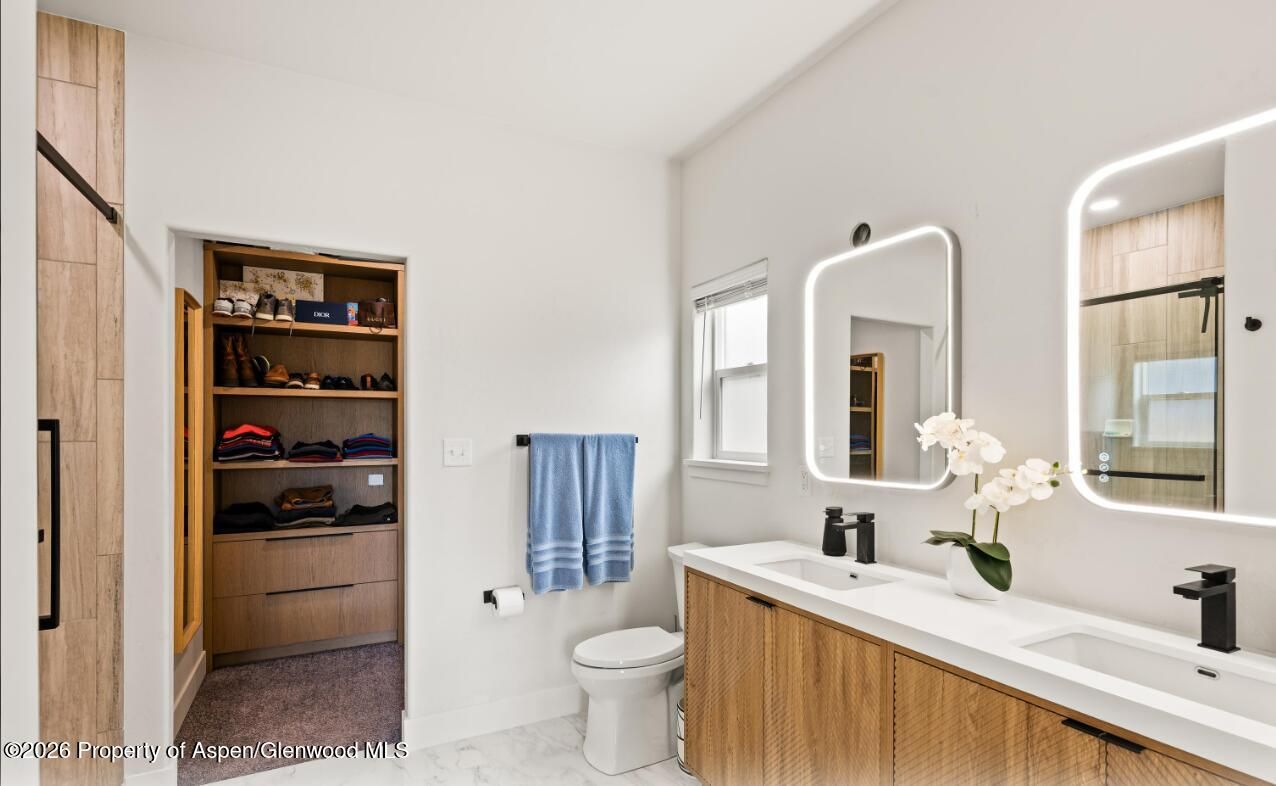 Modern bathroom with wood vanity, large mirror, shower, toilet, and open linen closet