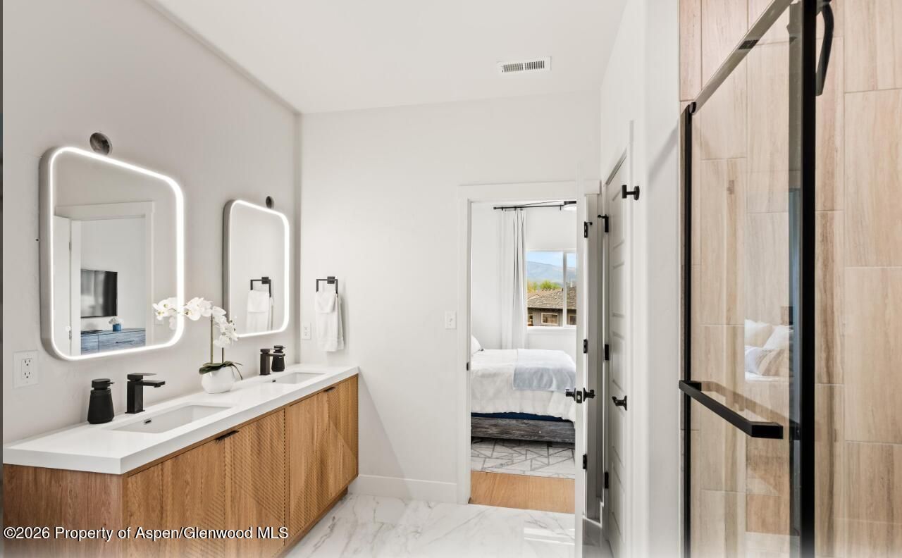 Modern bathroom with double wooden vanity, white sinks, mirrors, and a glass-enclosed shower