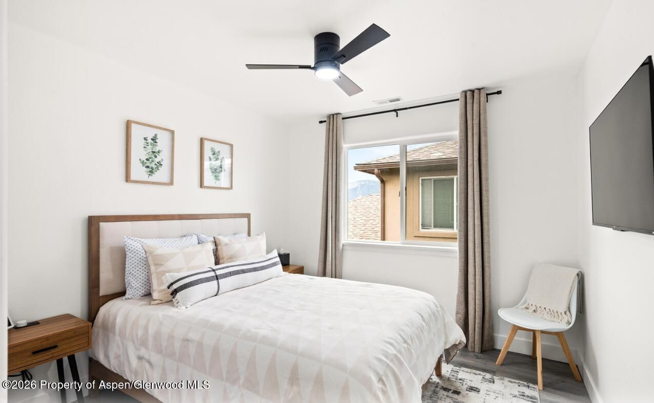 Bright bedroom with a white bed, framed wall art, window, chair, and ceiling fan