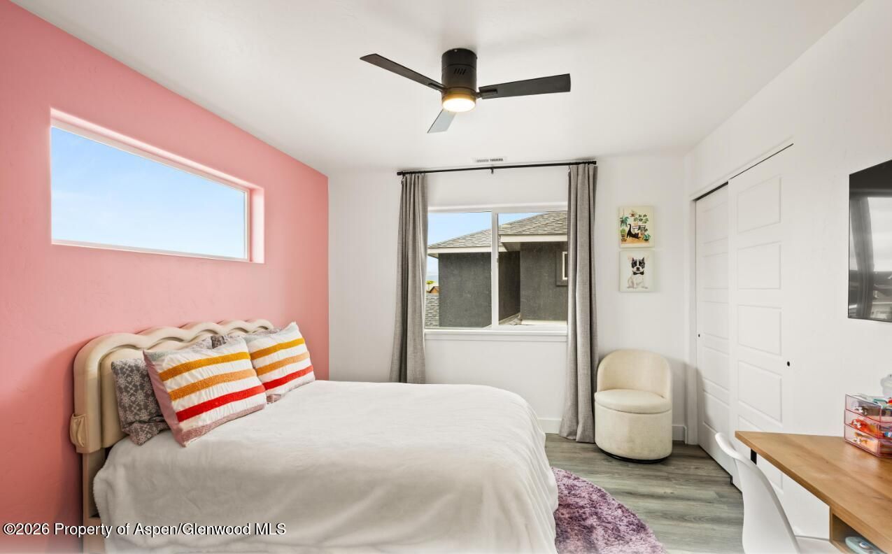 Bright bedroom with pink accent wall, white bed, ceiling fan, and window with curtains.
