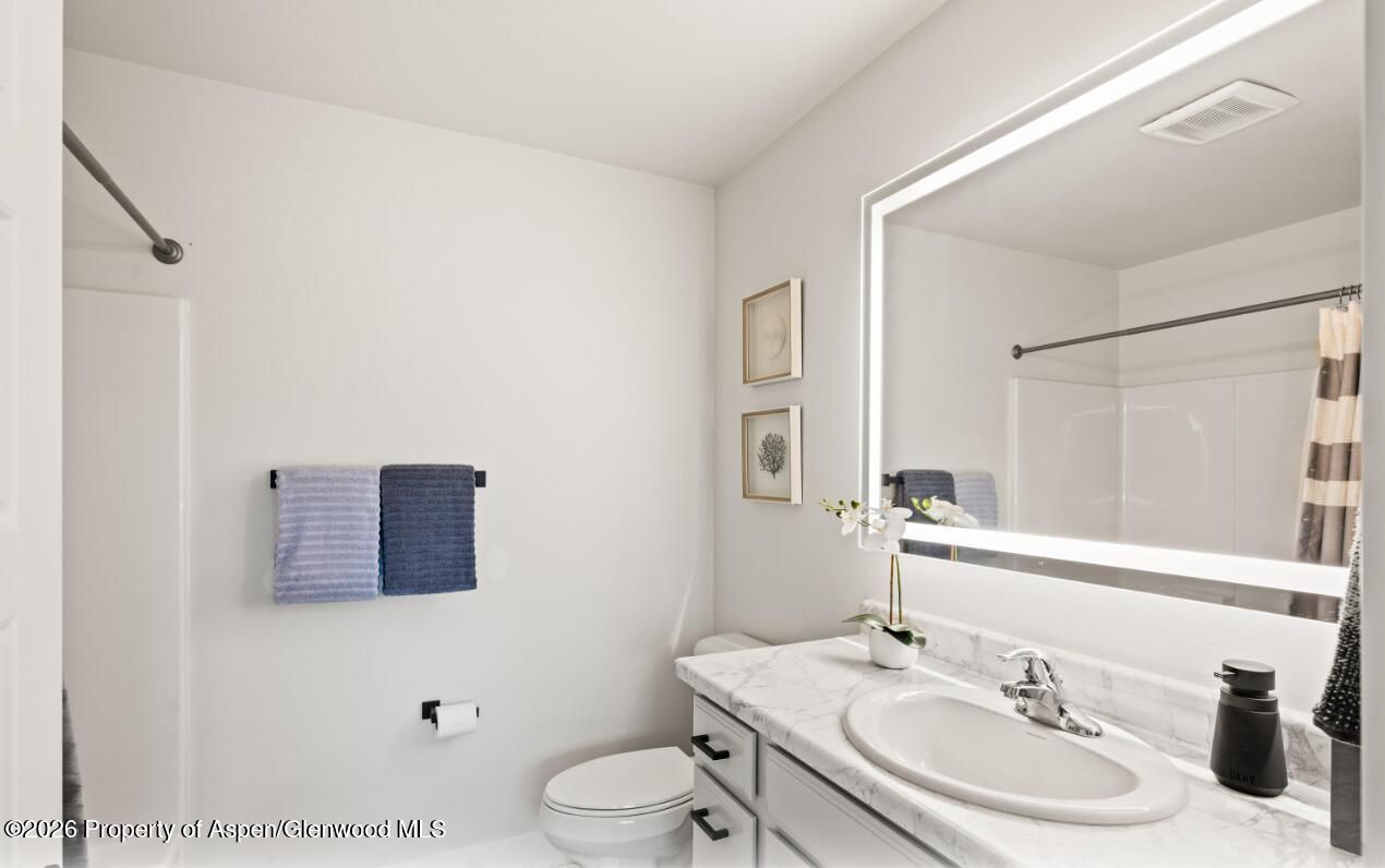Bright white bathroom with a sink, toilet, large mirror, and blue towels on the wall