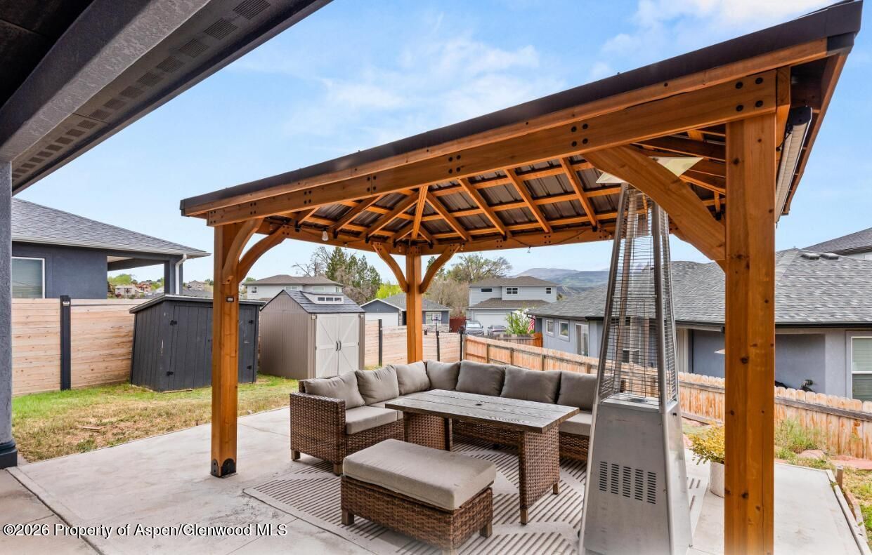 Covered backyard patio with a wooden gazebo, outdoor sofa, and rug beside a fenced yard.