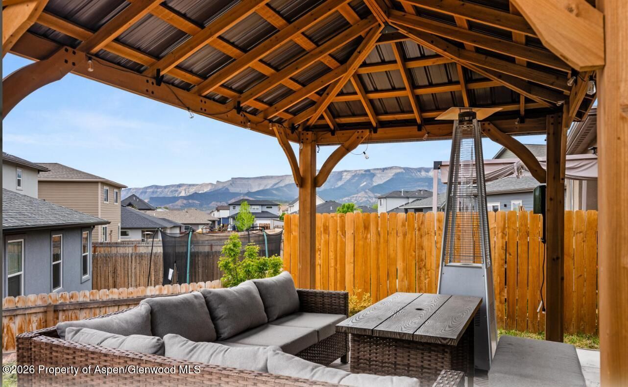 Covered backyard patio with gray sectional sofa, fire pit table, and mountain view beyond wooden fence