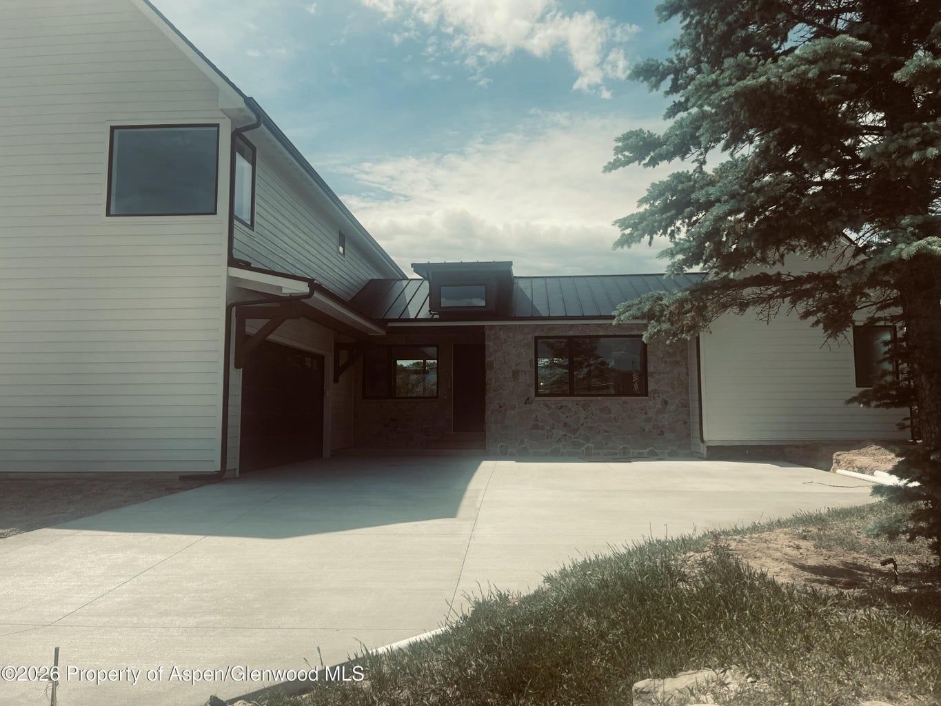 Two-story house with white siding, brick entry, and a concrete driveway under a partly cloudy sky.