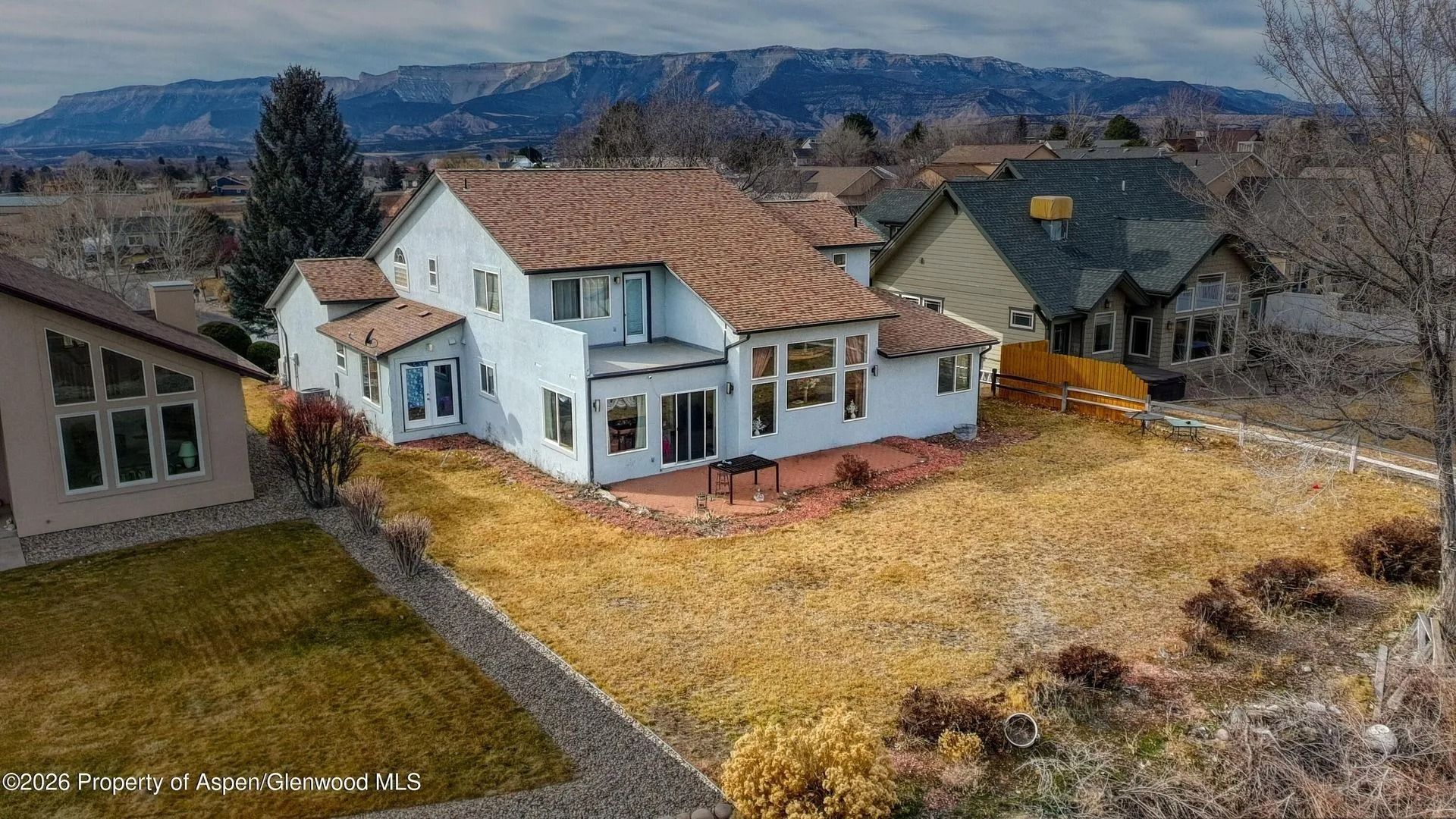 White two-story house with red roof and large yard in a suburban neighborhood, mountains in the background