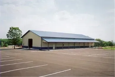 Large, rectangular building with blue roof and awning, beige walls, and empty parking lot.