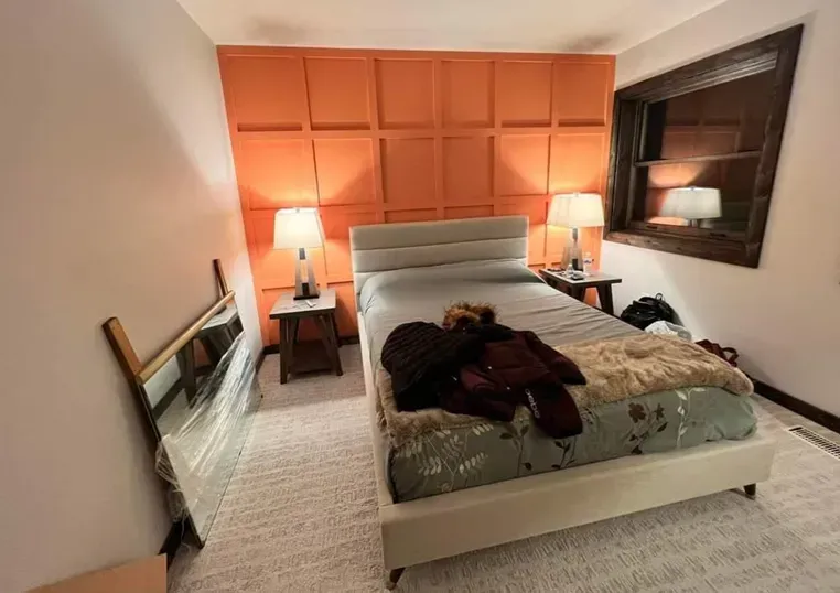 Orange textured wall behind a bed, flanked by tables with lamps; mirror leaning against a wall. Orange textured wall behind a bed, flanked by tables with lamps; mirror leaning against a wall.