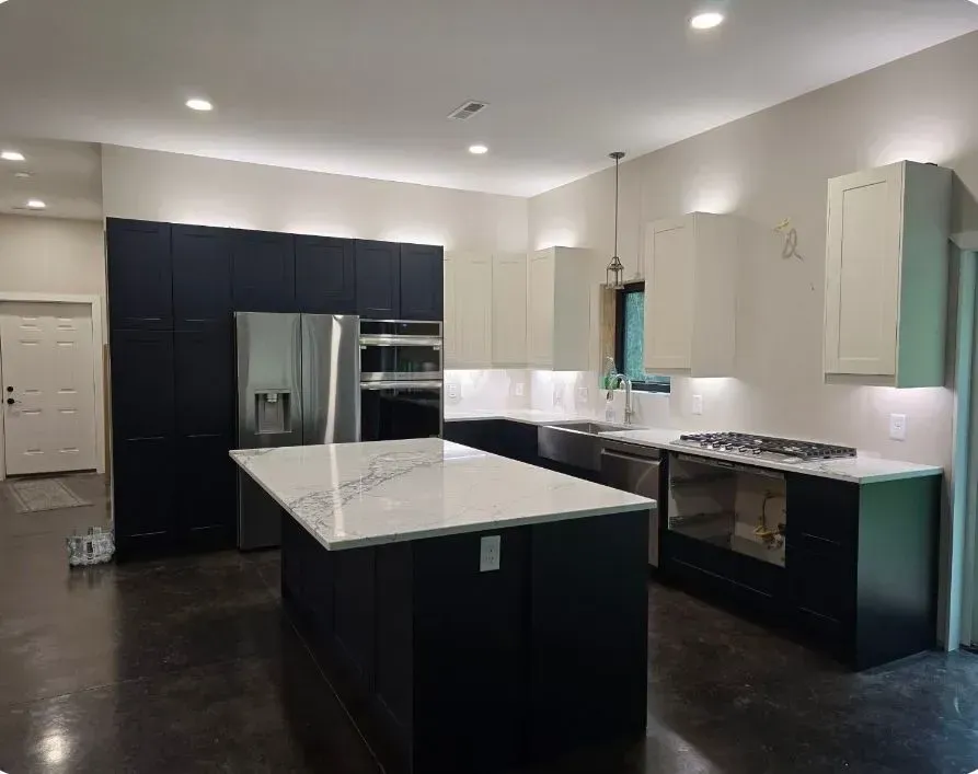 Modern kitchen with dark blue and white cabinets, stainless steel appliances, and a marble countertop island.