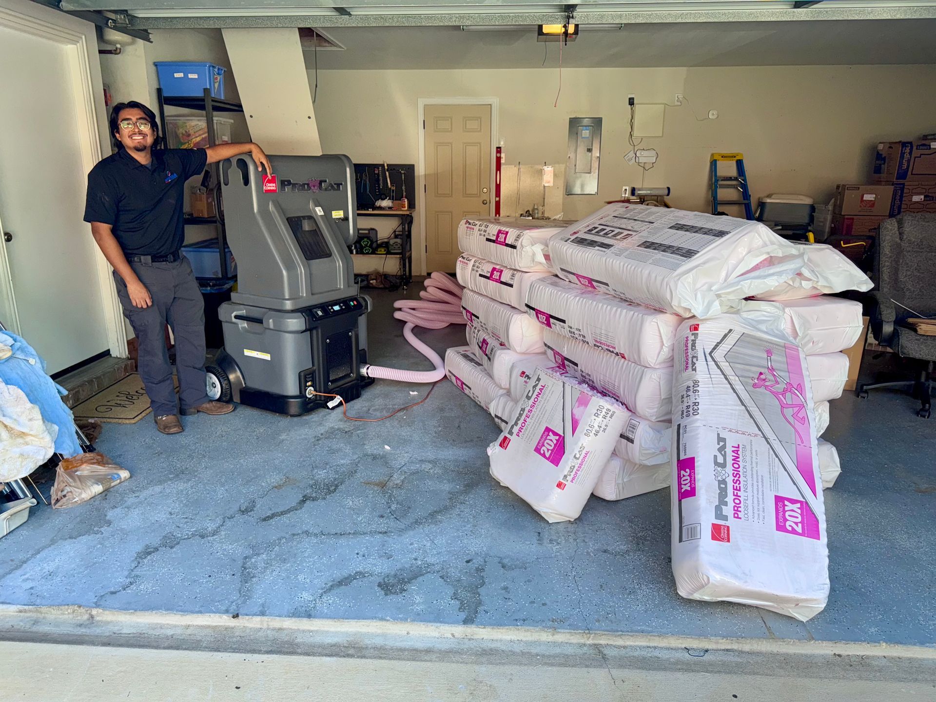 Man stands in a garage next to insulation and a machine. Garage is cluttered.