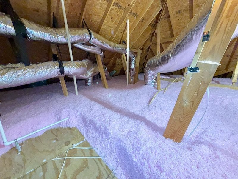 Pink insulation in an attic. Black ductwork and a temperature reading card are visible.