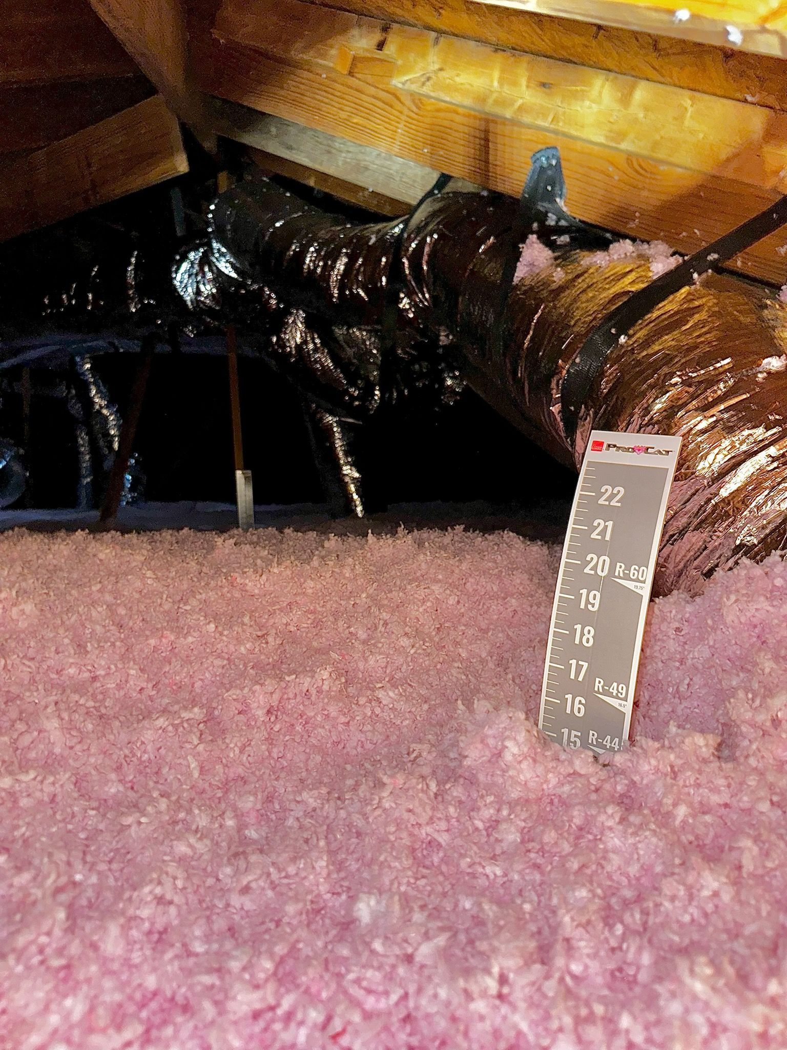 Pink insulation in an attic. Black ductwork and a temperature reading card are visible.