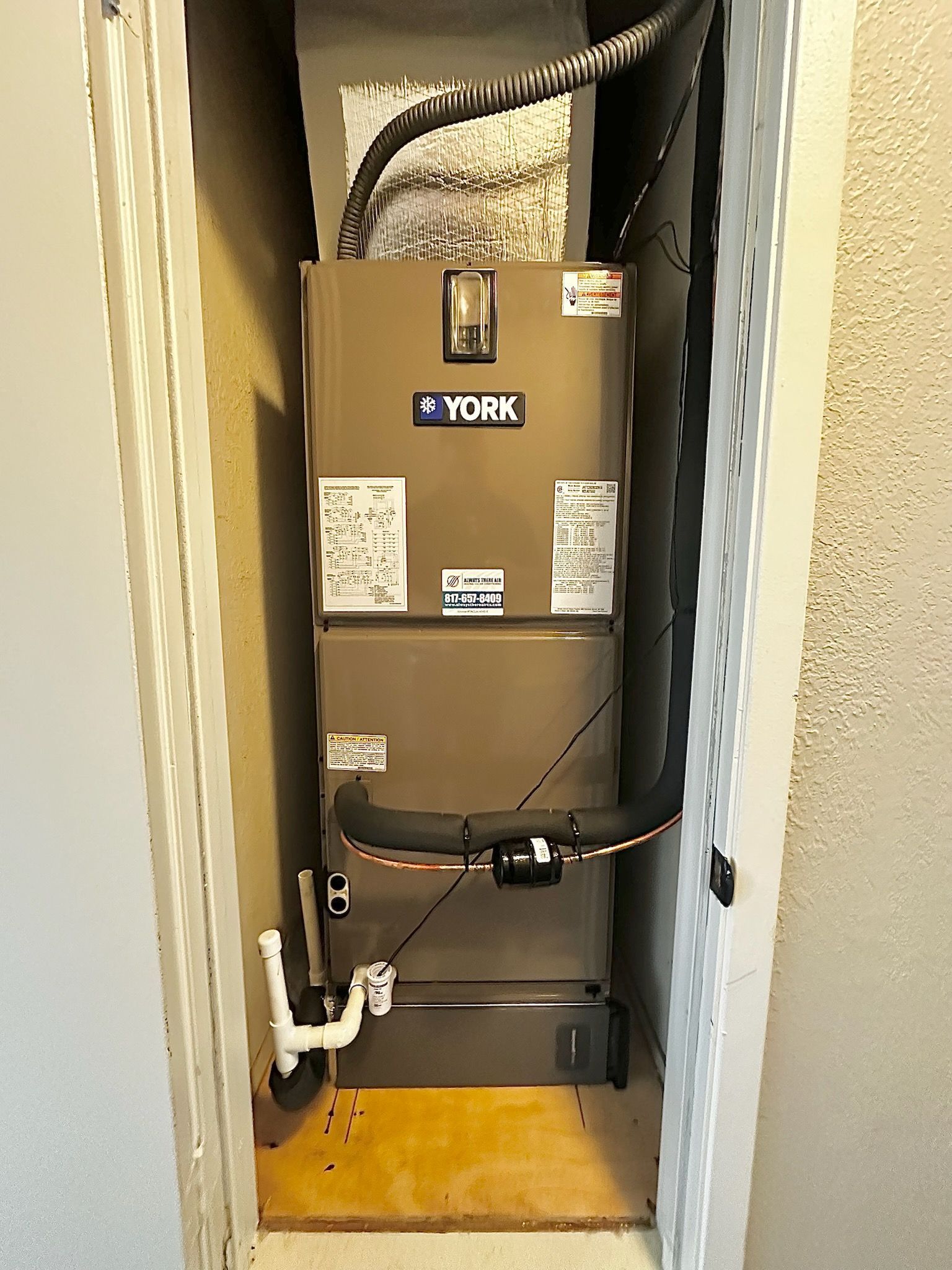 A York HVAC unit installed in a closet. Brown metal, black ductwork, white PVC pipes.