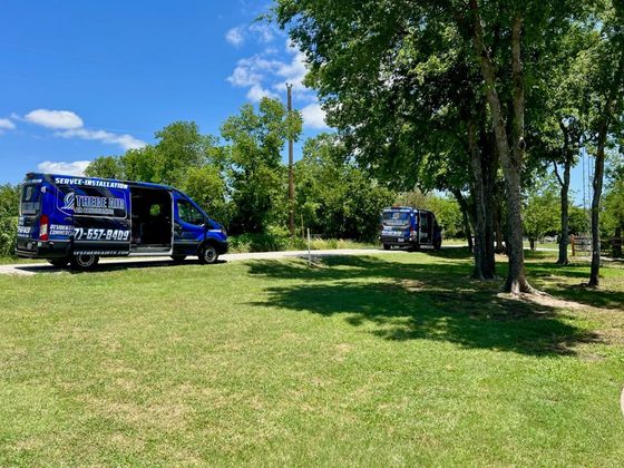Two blue vans with company logos parked on a grassy area under trees on a sunny day.