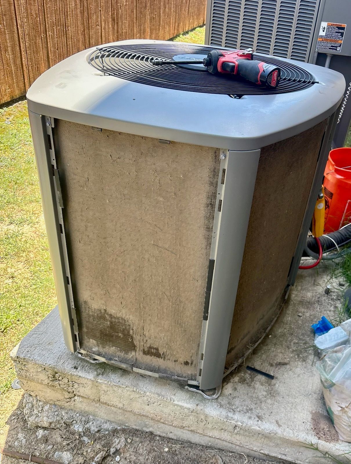 Dirty outdoor air conditioning unit on a concrete slab, with a screwdriver on top.