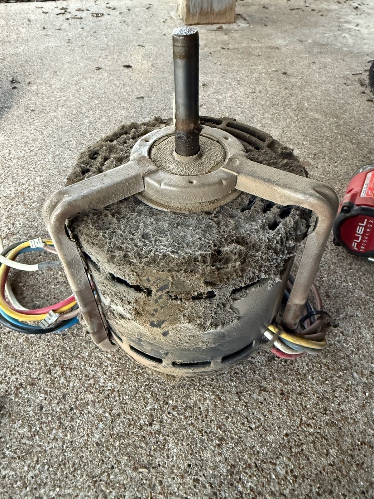 Motor covered in debris, with wires and a metal fan.