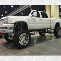 Lifted white pickup truck with large chrome wheels displayed indoors