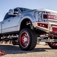 Lifted silver pickup truck with large off-road tires and red rims parked outdoors