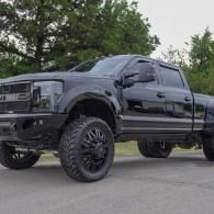 Black lifted pickup truck parked on pavement with trees in the background