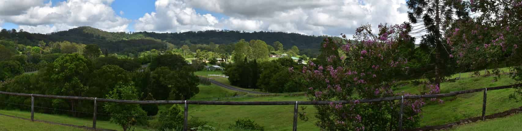 A Fence Surrounds a Grassy Field With Trees and Mountains — CTS Locksmiths in Nambour, QLD