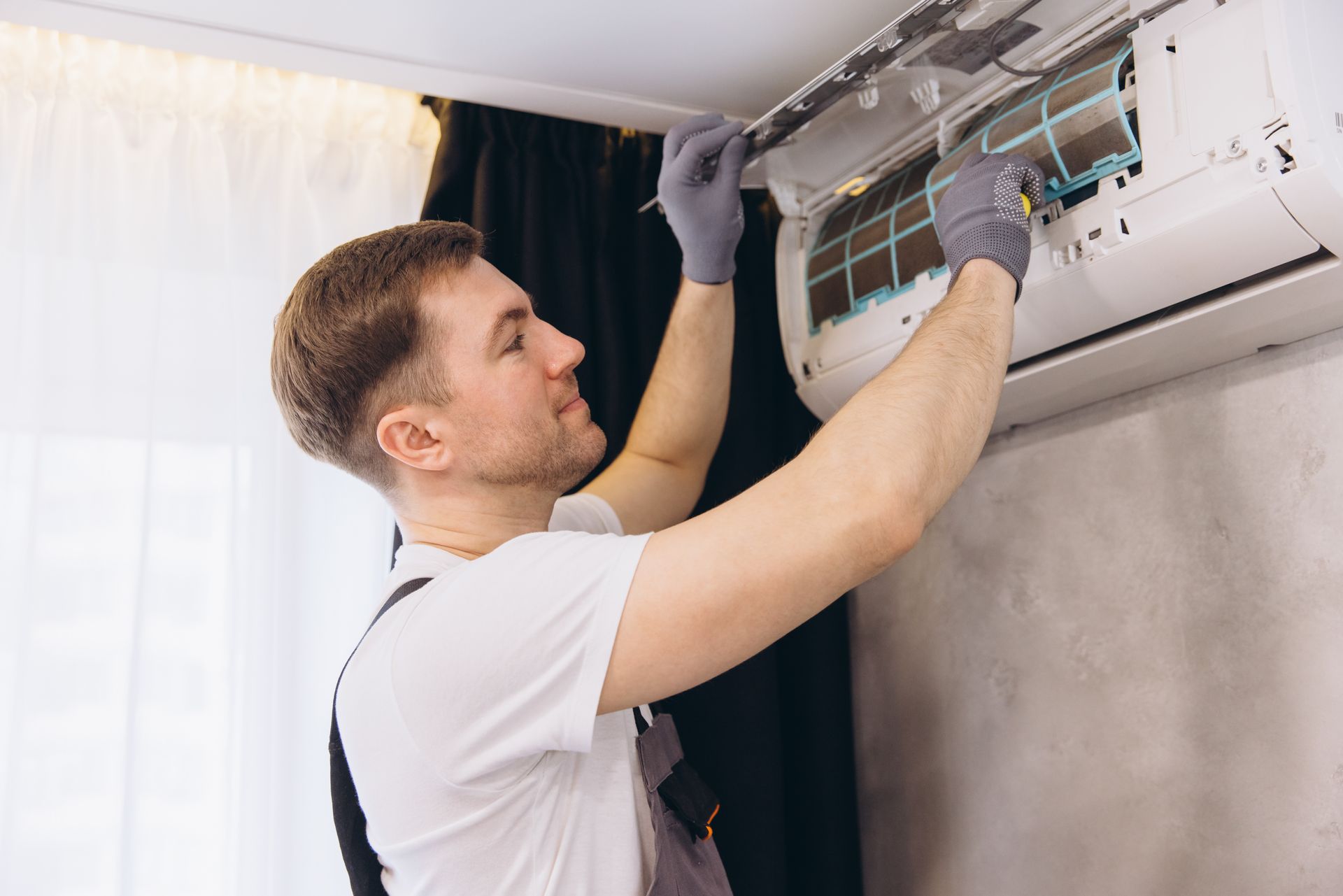 Technician servicing wall-mounted AC unit, inspecting filters and wiring.