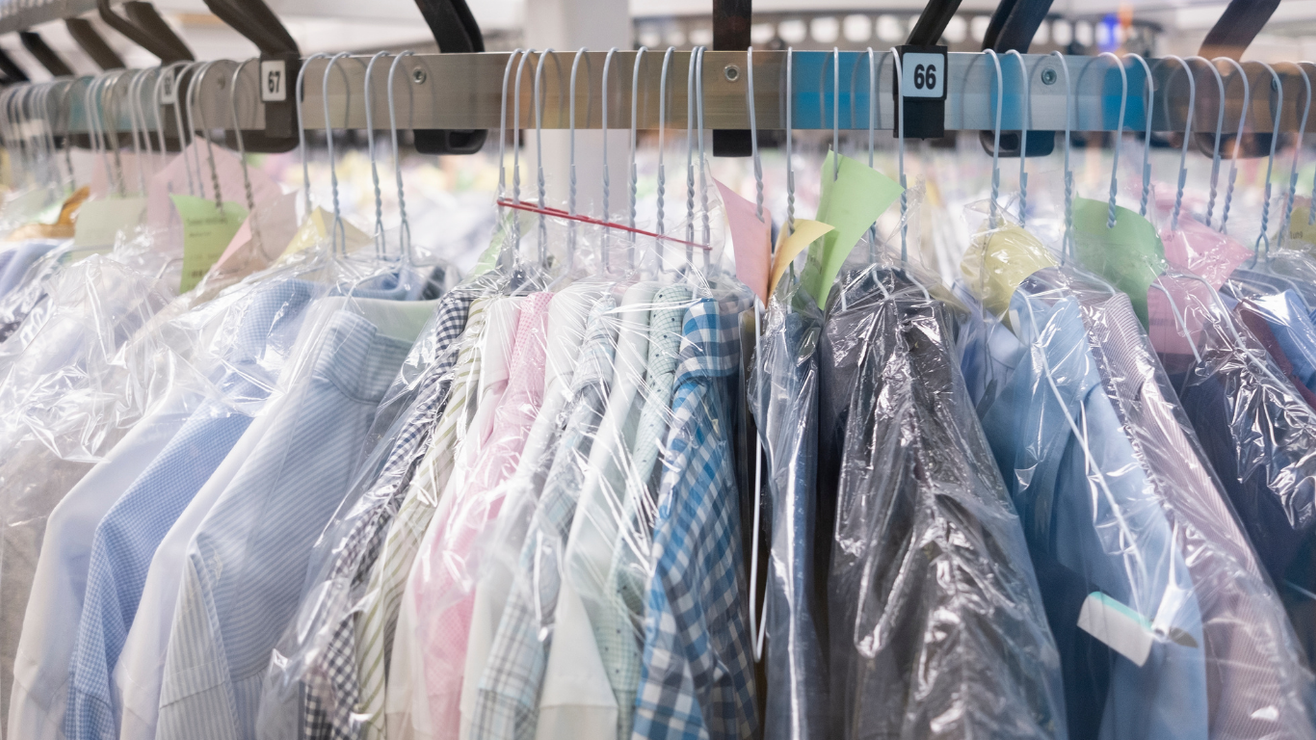 Rows of dry-cleaned shirts in plastic garment bags hang on a rack in a shop.
