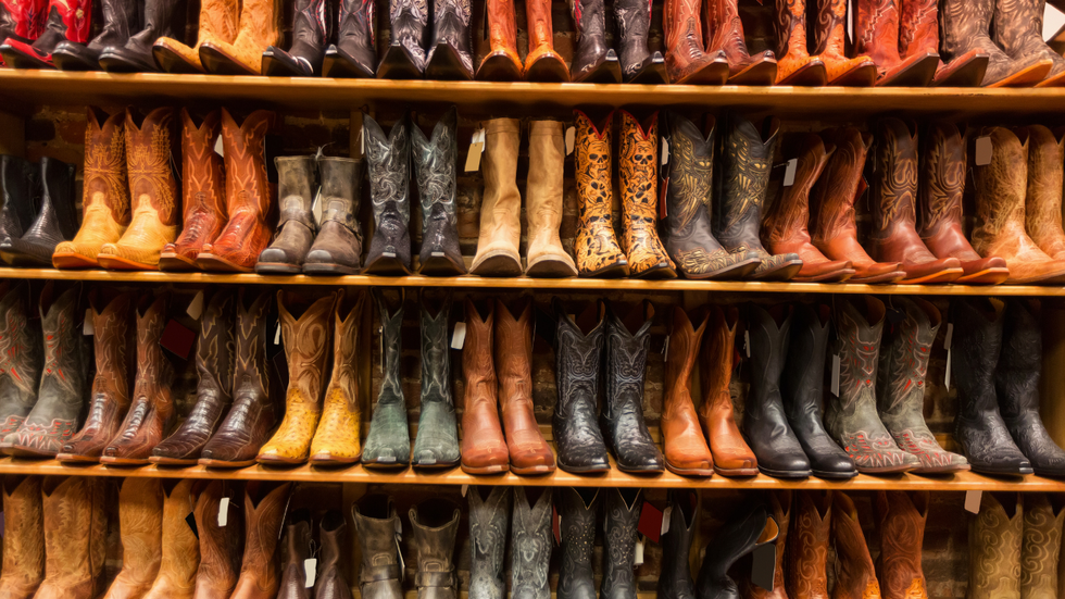 Rows of various leather cowboy boots on wooden shelves in a store.