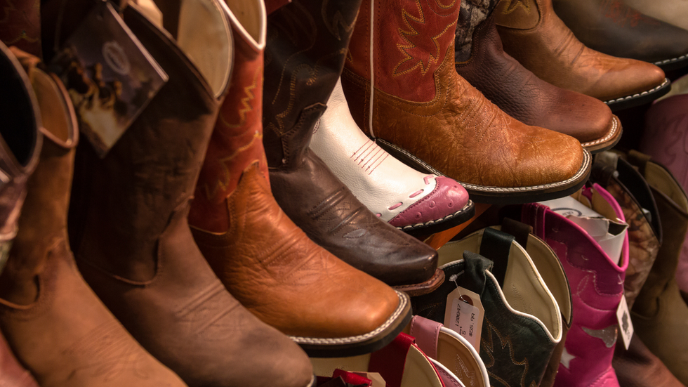 A shelf display of various leather cowboy boots in shades of brown, white, and pink, seen from a high angle.