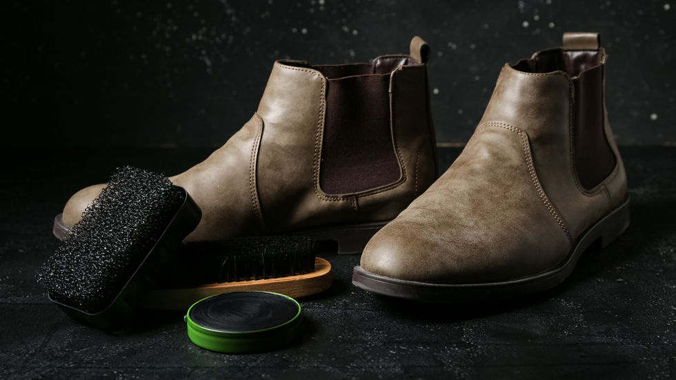 A pair of tan Chelsea boots with a shoe brush and polish tin on a dark, textured surface.