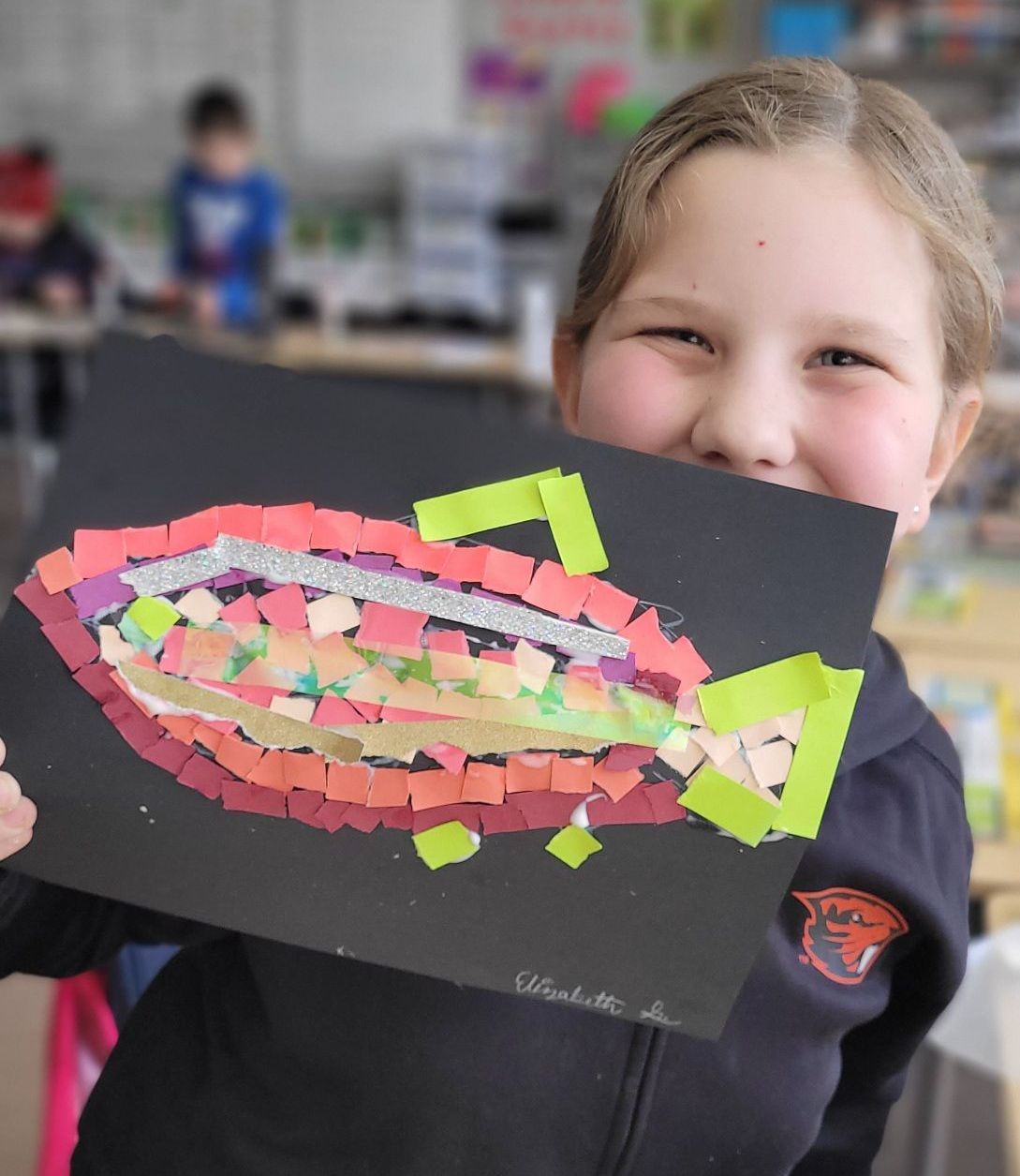 A young girl is holding a piece of paper with a fish on it