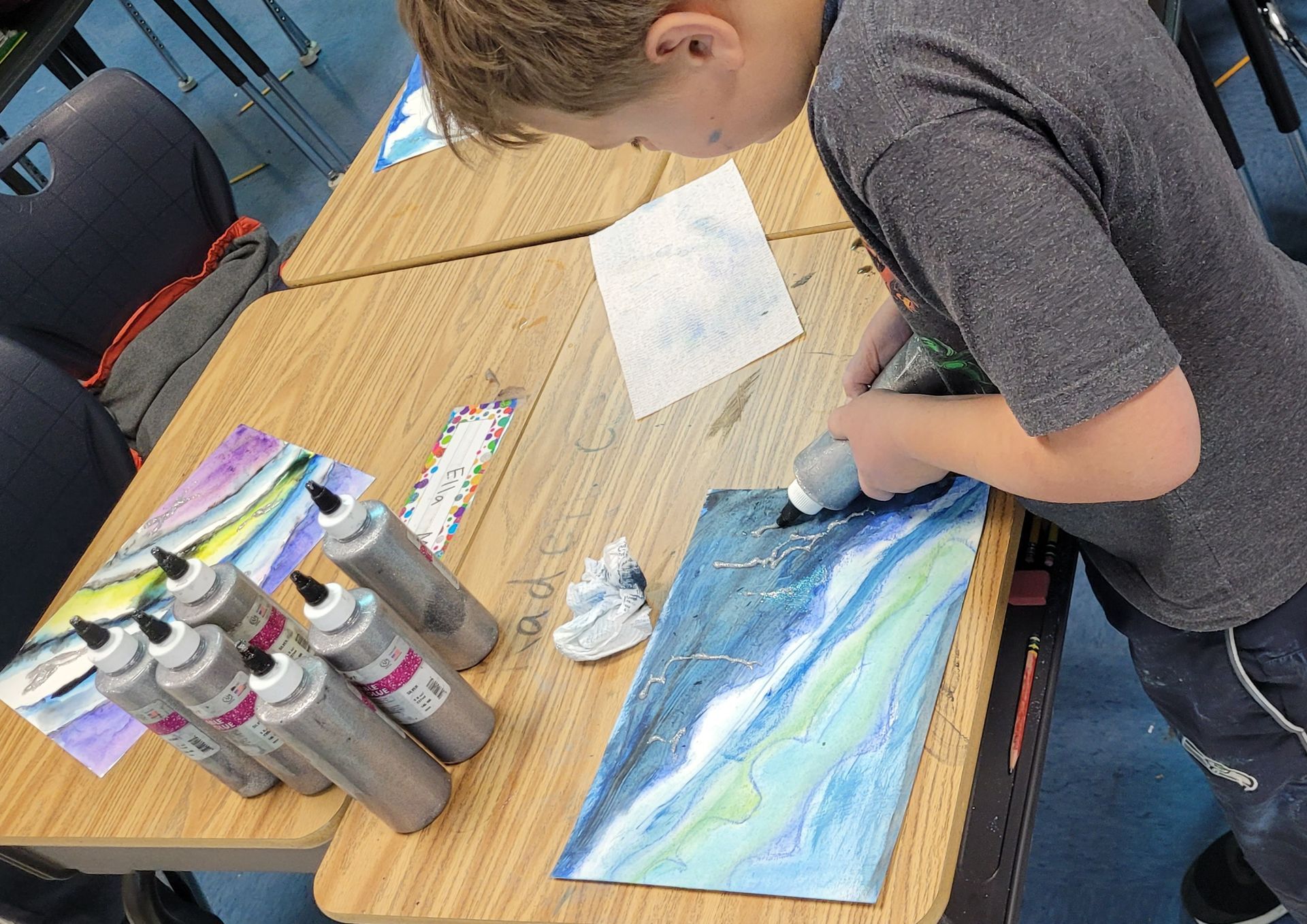 A young boy is sitting at a table painting a picture.